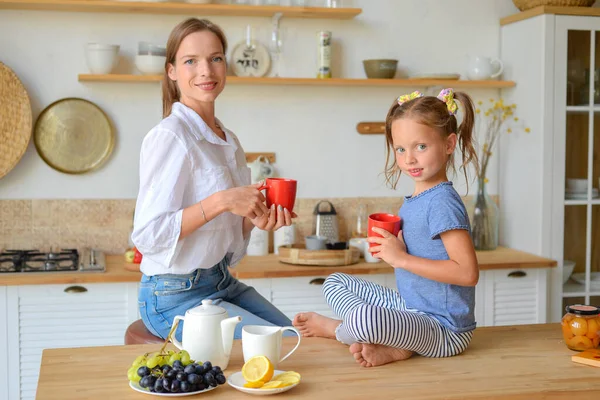 Mutlu anne ve küçük kız birlikte sıcak çay içip evde kahvaltı ediyorlar.