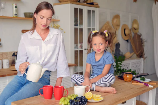 Anne ve küçük kızı mutfakta çay içip birlikte kahvaltı ediyorlar. aile portresi