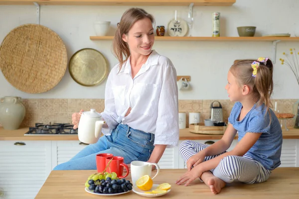 Anne ve küçük kızı mutfakta çay içip birlikte kahvaltı ediyorlar. aile portresi