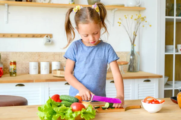 Mutfaktaki küçük kız salata için sebze kesiyor. Doğru beslenme ve vejetaryenlik kavramı