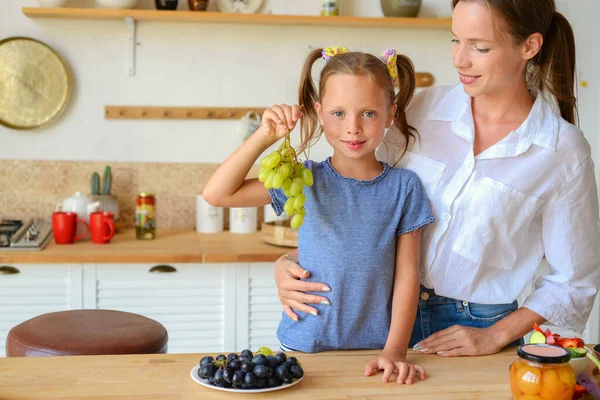 Annesiyle birlikte mutfakta üzüm yiyen tatlı bir kız.