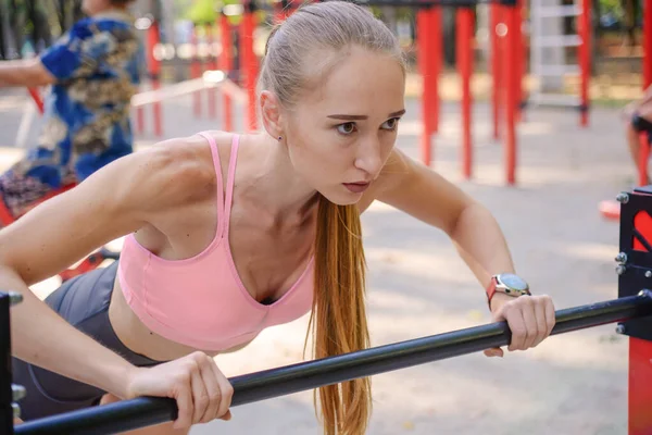Aktif yaşam tarzı. Sıska esmer kadın antrenman yapıyor. Güneşli yaz gününde dışarıda spor salonunda direniş bandıyla barfiks çekiyor..
