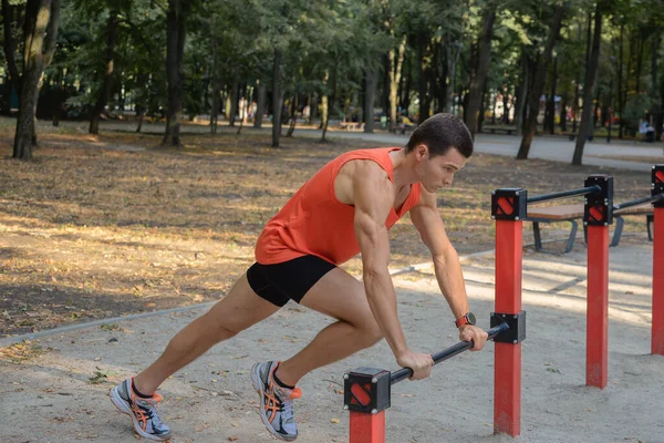 Atletik güçlü adam parkta sokak makineleri ve yatay barlarla antrenman yapıyor.