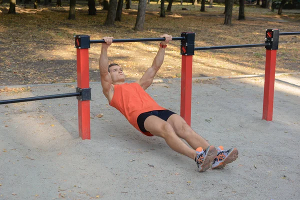 Atletik güçlü adam parkta sokak makineleri ve yatay barlarla antrenman yapıyor.