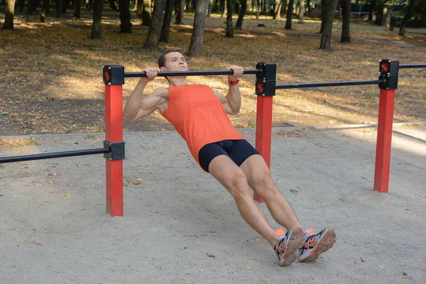 Atletik güçlü adam parkta sokak makineleri ve yatay barlarla antrenman yapıyor.