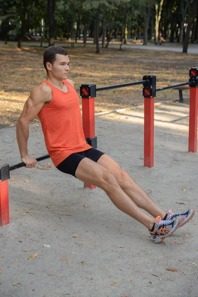 Atletik güçlü adam parkta sokak makineleri ve yatay barlarla antrenman yapıyor.