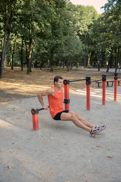 Atletik güçlü adam parkta sokak makineleri ve yatay barlarla antrenman yapıyor.