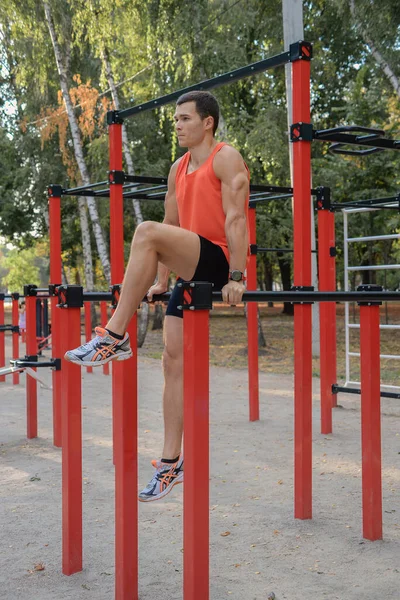 Atletik güçlü adam parkta sokak makineleri ve yatay barlarla antrenman yapıyor.