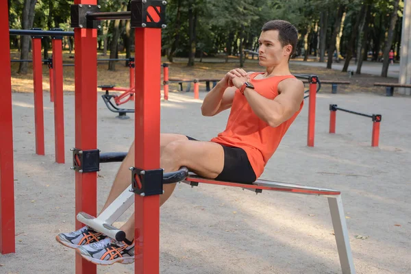 Atletik güçlü adam parkta sokak makineleri ve yatay barlarla antrenman yapıyor.