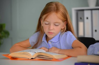 Okula geri dönüyoruz. Mutlu gülümseyen kız masada okuyor ve yazıyor. Sınıftaki çocuk