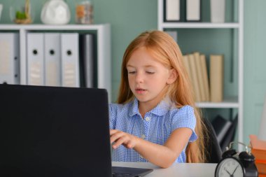 Koronavirüs salgını nedeniyle karantina sırasında internetten alınan bir derste evde dizüstü bilgisayarla oturan bir ilkokul öğrencisi.