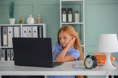 Koronavirüs salgını nedeniyle karantina sırasında internetten alınan bir derste evde dizüstü bilgisayarla oturan bir ilkokul öğrencisi.