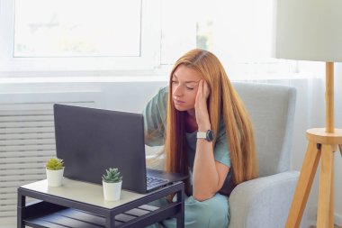 Evde dizüstü bilgisayarla çalışan genç bir kadın.