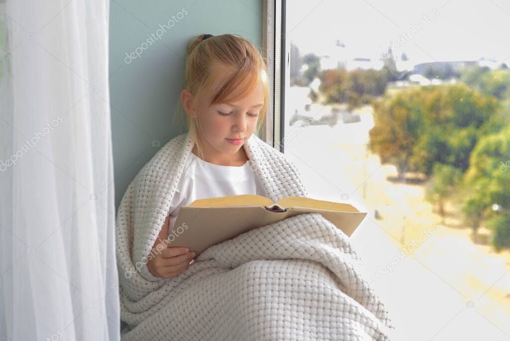 cute girl schoolgirl reading a book by the window at home