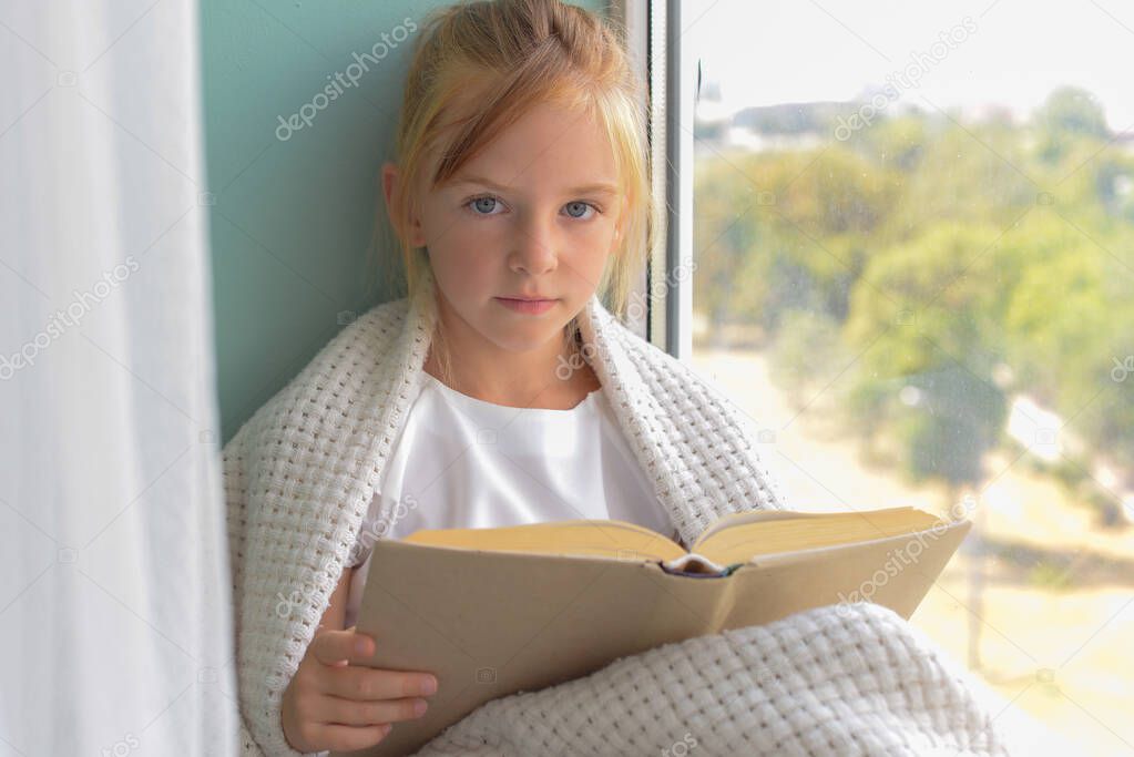 cute girl schoolgirl reading a book by the window at home