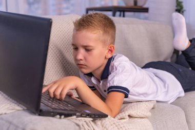 Kulaklıklı çocuk dizüstü bilgisayar kullanıyor ve evdeki video öğretmeniyle internetten ders çalışıyor. Evde eğitim, uzak öğrenim