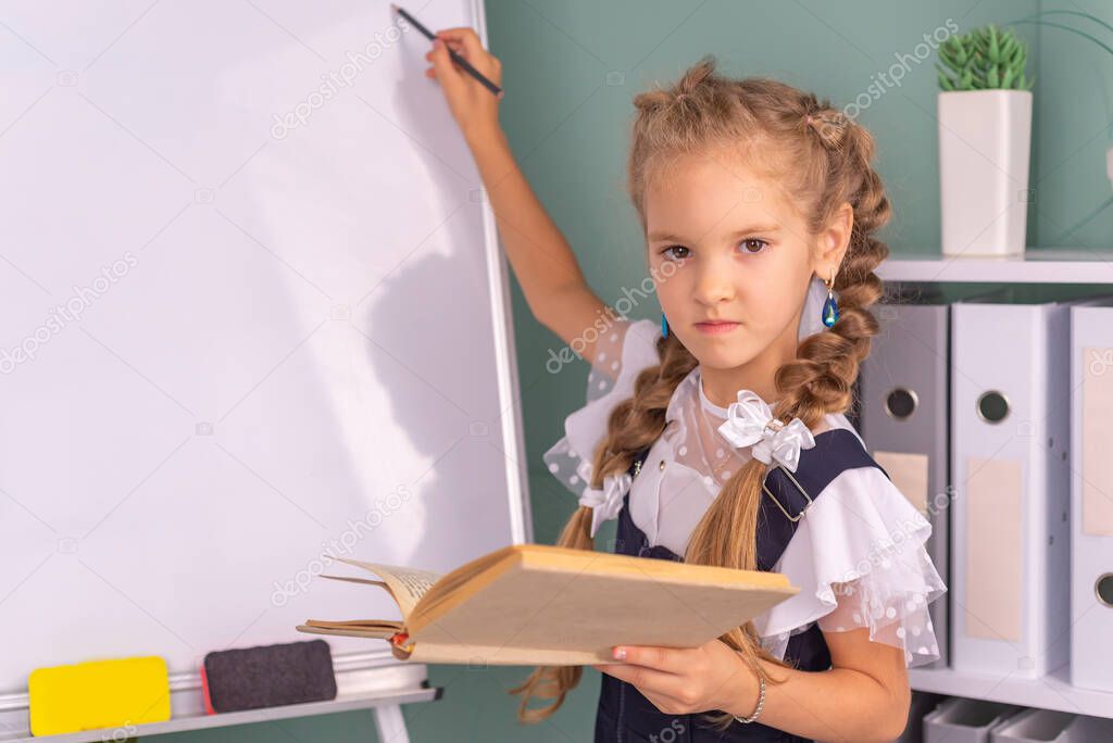 Back to school and happy time! A cute hardworking child is sitting at a table indoors. girl studying in the classroom on the background of the blackboard. The girl is reading a book.