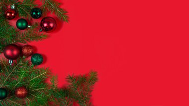 Vibrant and colorful Christmas ornaments elegantly resting on lush pine branches against a bold red backdrop