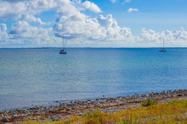 Pebbled Beach 'in yanında iki yelkenli, kıyıda hafif dalgalar, dağılmış bulutlarla aydınlık gökyüzü, dengeli bileşim...