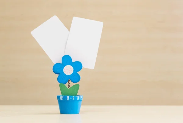 Closeup clamp photo in blue flower shape shape in flowerpot with black white paper on blurred wooden desk and wall background