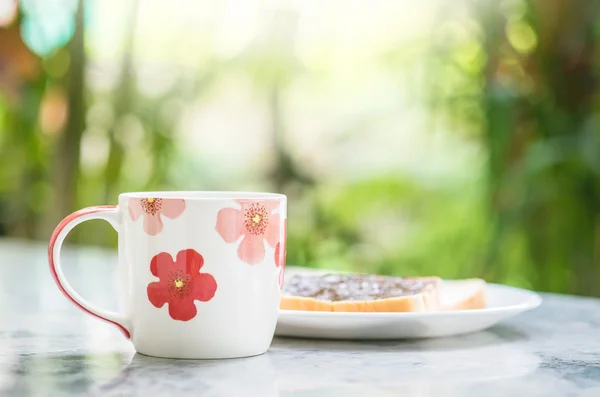 Nahaufnahme niedliche Tasse auf verschwommenem Marmor Schreibtisch und Blick auf den Garten am Morgen strukturierten Hintergrund — Stockfoto