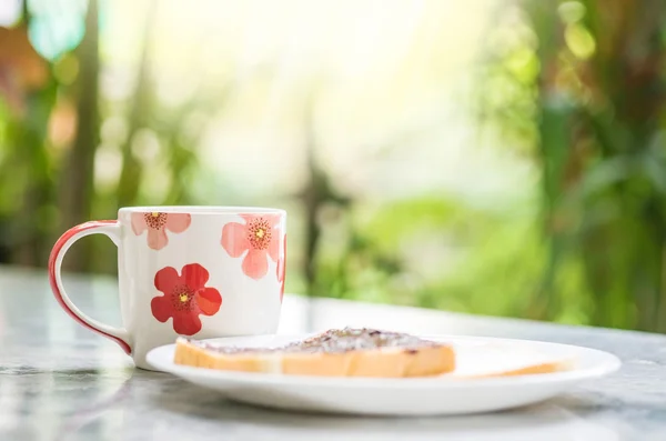 Nahaufnahme niedliche Tasse auf verschwommenem Marmor Schreibtisch und Blick auf den Garten am Morgen strukturierten Hintergrund — Stockfoto