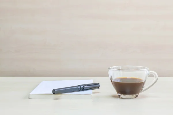 흰색 책에 검은 색 펜을 닫아 서 투명 한 나무 책상에 커피의 투명 한 컵에 검은 커피와 창 아래 회의실에서 벽 질감 배경 — 스톡 사진