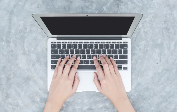 Primeros planos de la mujer escribiendo a mano en el teclado en el ordenador portátil gris en el escritorio de hormigón fondo texturizado en el jardín, el trabajo en el concepto al aire libre — Foto de Stock