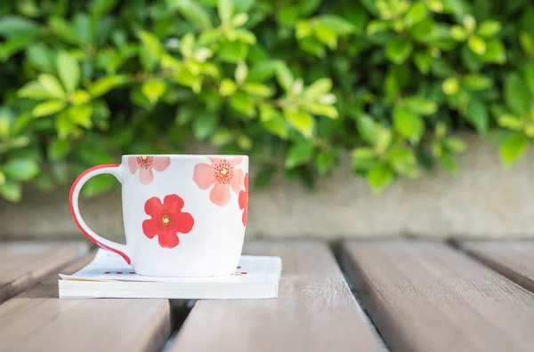 Nahaufnahme schöne Tasse Kaffee auf weißem Buch auf verschwommenem Holztisch und grüne Pflanze im Garten strukturierten Hintergrund, Entspannungskonzept mit netter Tasse und Buch — Stockfoto