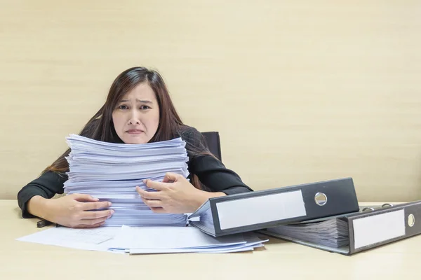 Closeup working woman working with document file and pile of work paper in boring emotion concept on blurred wooden desk and wall textured background in the meeting room under window light