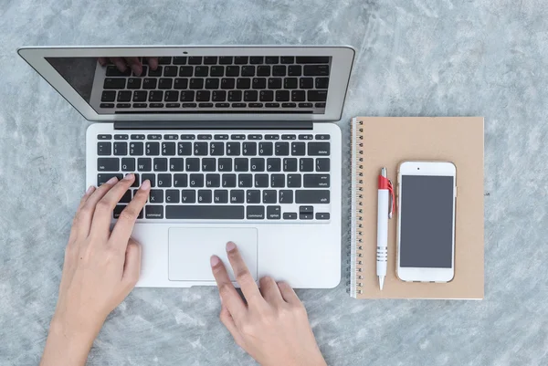 Primeros planos mujer tecleando a mano en el teclado en el ordenador portátil gris en el escritorio de hormigón fondo texturizado bajo la luz del día en el jardín en la vista superior, concepto de trabajo al aire libre — Foto de Stock