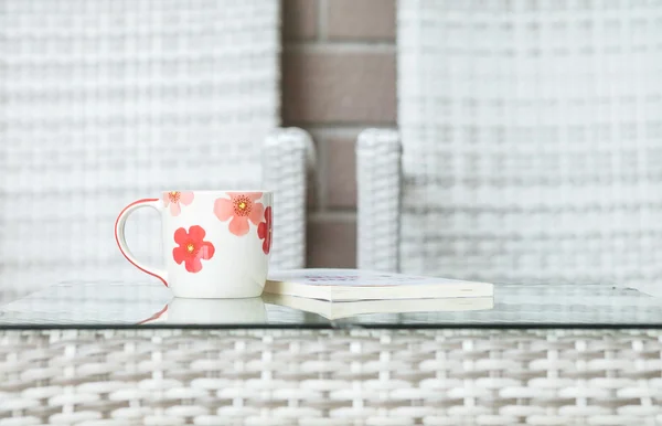 Nahaufnahme niedliche Tasse auf verschwommenem Buch und Holz weben Tisch und Stuhl strukturierten Hintergrund — Stockfoto