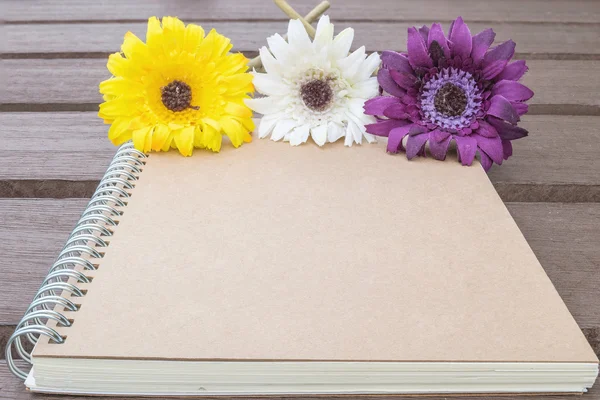Closeup hnědá kniha s barevnou předstaženou květinou na rozmazaných starých dřevěných tabulí pozadí s texturou — Stock fotografie