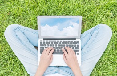 Asya kadın dizüstü ekranda mavi gökyüzü ile bir dizüstü bilgisayar kullanmak için bahçe dokulu arka plan çim zemin üzerinde oturan , açık havada iş konsepti