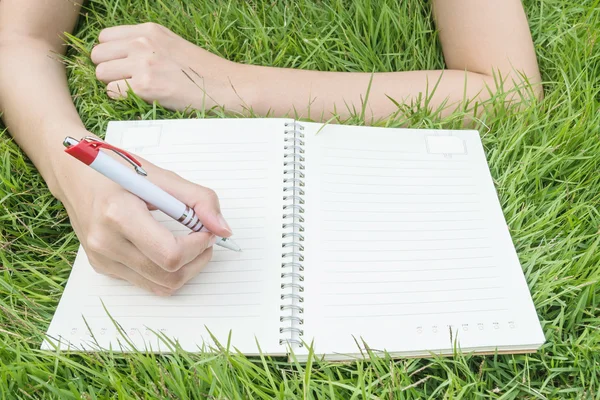 Primer plano mujer asiática acostada en el campo de hierba texturizado fondo para escribir en el cuaderno bajo la luz del día en el jardín — Foto de Stock