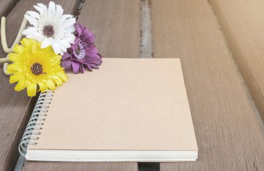 Bulanık eski ahşap masa dokulu arka plan üzerinde renkli sahte çiçek ile Closeup kahverengi not defteri