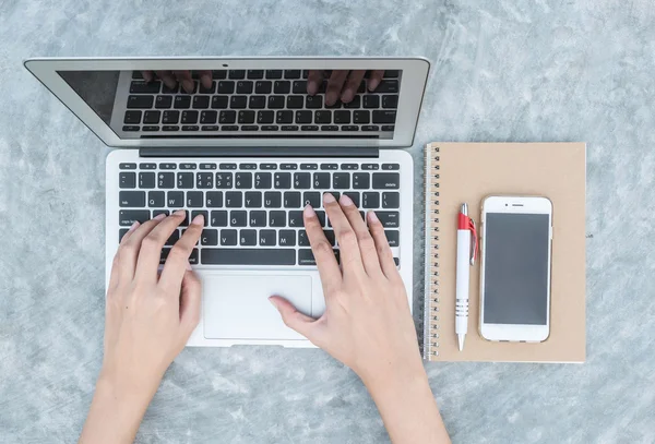 Primeros planos mujer tecleando a mano en el teclado en el ordenador portátil gris en el escritorio de hormigón fondo texturizado bajo la luz del día en el jardín en la vista superior, concepto de trabajo al aire libre — Foto de Stock