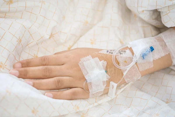 Closeup saline water line at the hand of patient on bed in hospital room