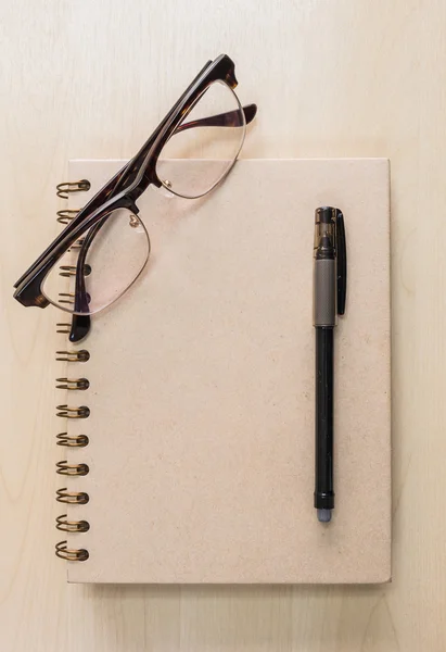 Cuaderno marrón con gafas y bolígrafo negro sobre fondo de madera — Foto de Stock