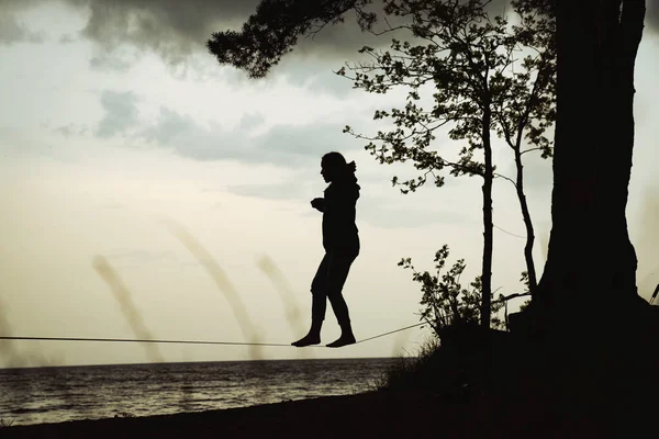 Lady practising slack line in the city park. Slacklining is a practice in balance that typically uses nylon or polyester webbing tensioned between two anchor points.