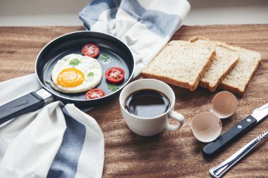 Kahve, sahanda yumurta, domates, ahşap tabakta ekmek. Masada nefis bir kahvaltı.