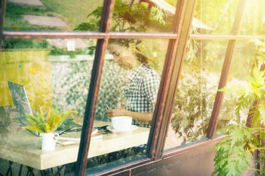 Kafe masasında oturan ve dizüstü bilgisayarla çalışan genç bir kadın. Kafedeki Asyalı kadın beyaz bardak ve kitapla dizüstü bilgisayar kullanıyor. Nesnelerin interneti teknoloji iletişim ağı kavramı