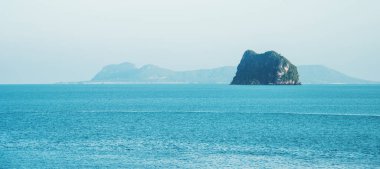 Uzaktaki Asya Tayland, mavi gökyüzü beyaz bulut ve okyanus dalgalarıyla uçsuz bucaksız yatay ve yalnız deniz. Arka planda dağ tepeleri var. seyahat doğa tatil açık hava konsepti