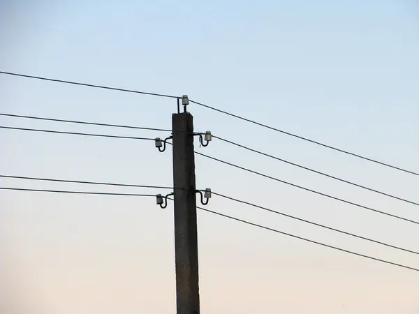 Akşam gökyüzünün arka planında elektrik kabloları olan bir direk.