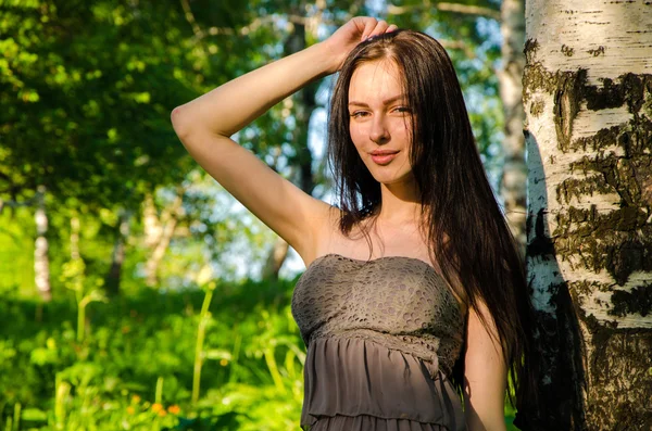 Brunette stands near the birch in forest. — Stock Photo, Image