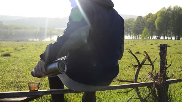 Mężczyzna Siedzący Drewnianym Skomeyke Nalewający Sobie Herbaty Termosu — Wideo stockowe