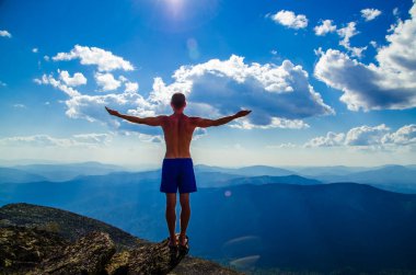 Adam bir dağın tepesinde elleri açık duruyor. Dağın tepesinde, kolları açık bir adam..