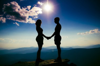 Bir dağın tepesinde el ele tutuşan sevgi dolu bir çift. Bir erkek ve bir kız birbirlerine dik dik bakarlar.