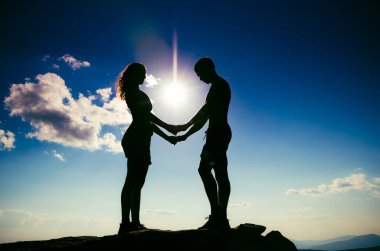 Bir dağın tepesinde el ele tutuşan sevgi dolu bir çift. Bir erkek ve bir kız birbirlerine dik dik bakarlar.