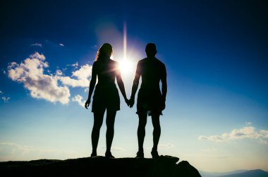 Bir dağın tepesinde el ele tutuşan sevgi dolu bir çift. Bir erkek ve bir kız birbirlerine dik dik bakarlar.